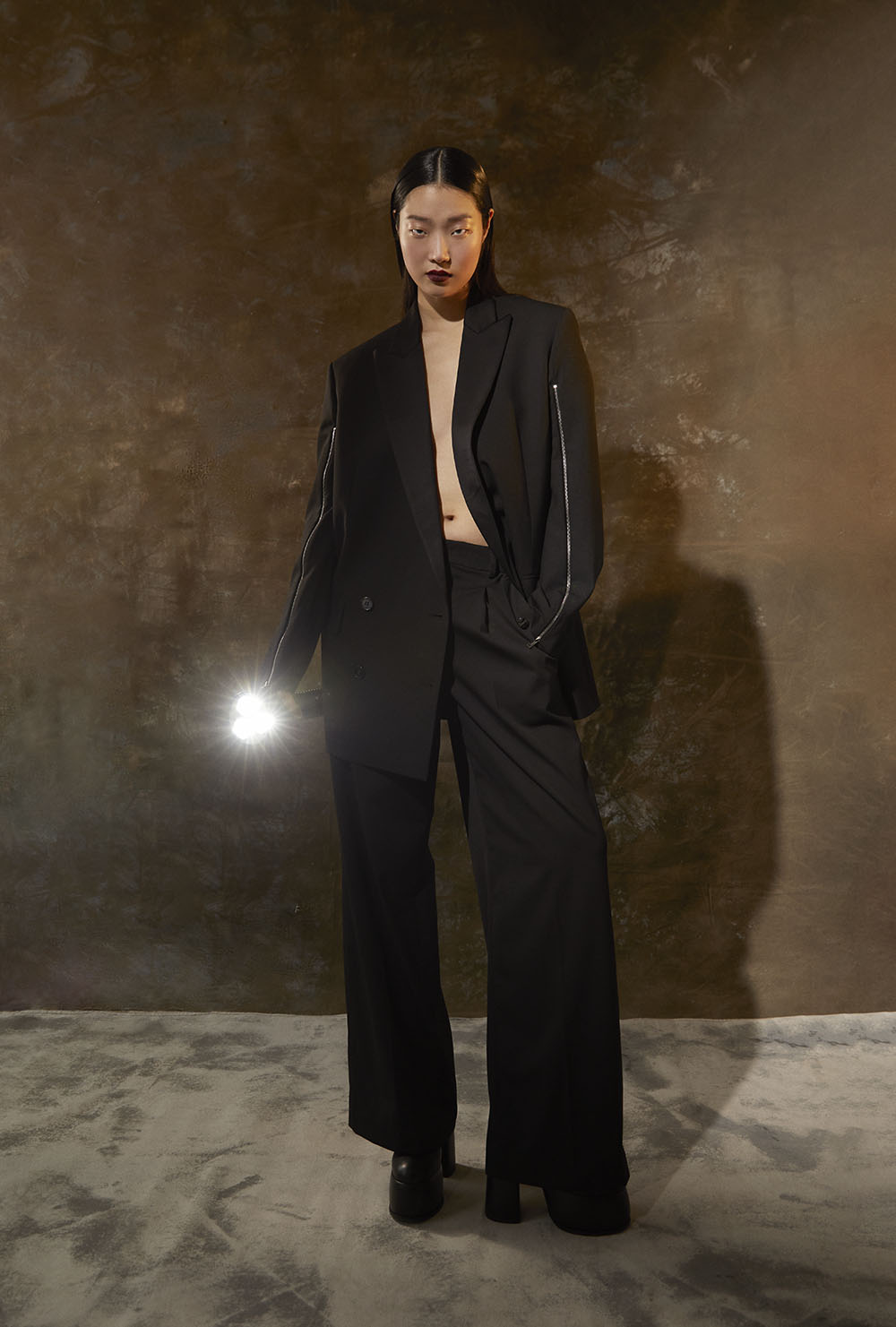 Best NYC fashion photographer - Model in oversized black suit holding flashlight with dramatic lighting in studio editorial by Vikram Pathak 