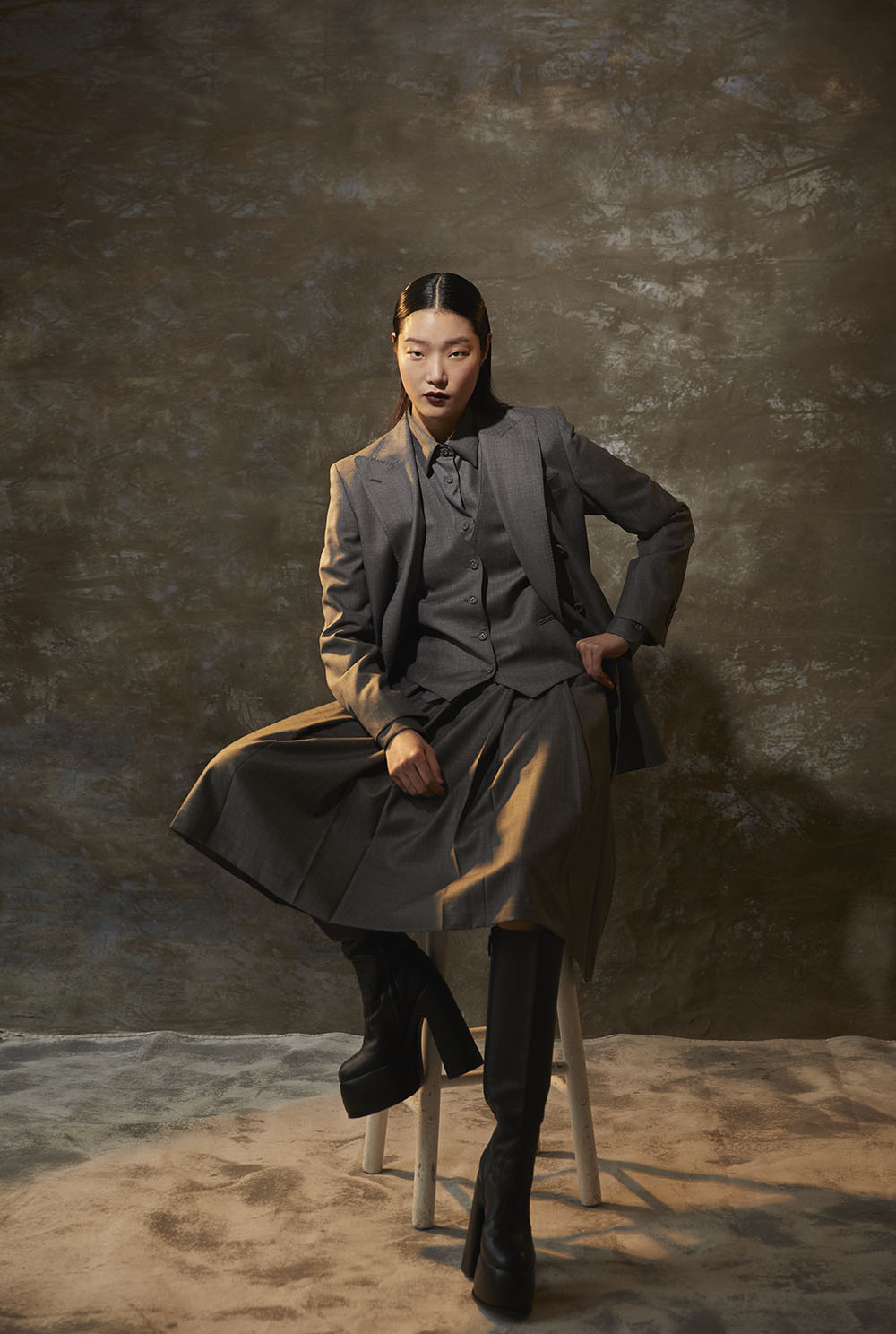 New York fashion Photographer -Model wearing tailored gray suit with pleated skirt and black boots in New York fashion studio editorial by Vikram Pathak