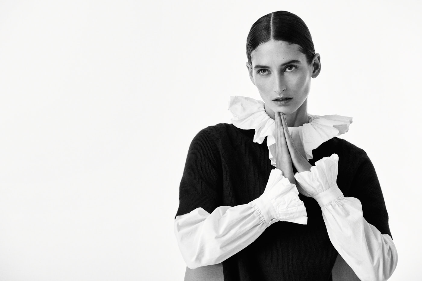 Black and white portrait of model in ruffled collar shirt with prayer pose – NYC fashion editorial
