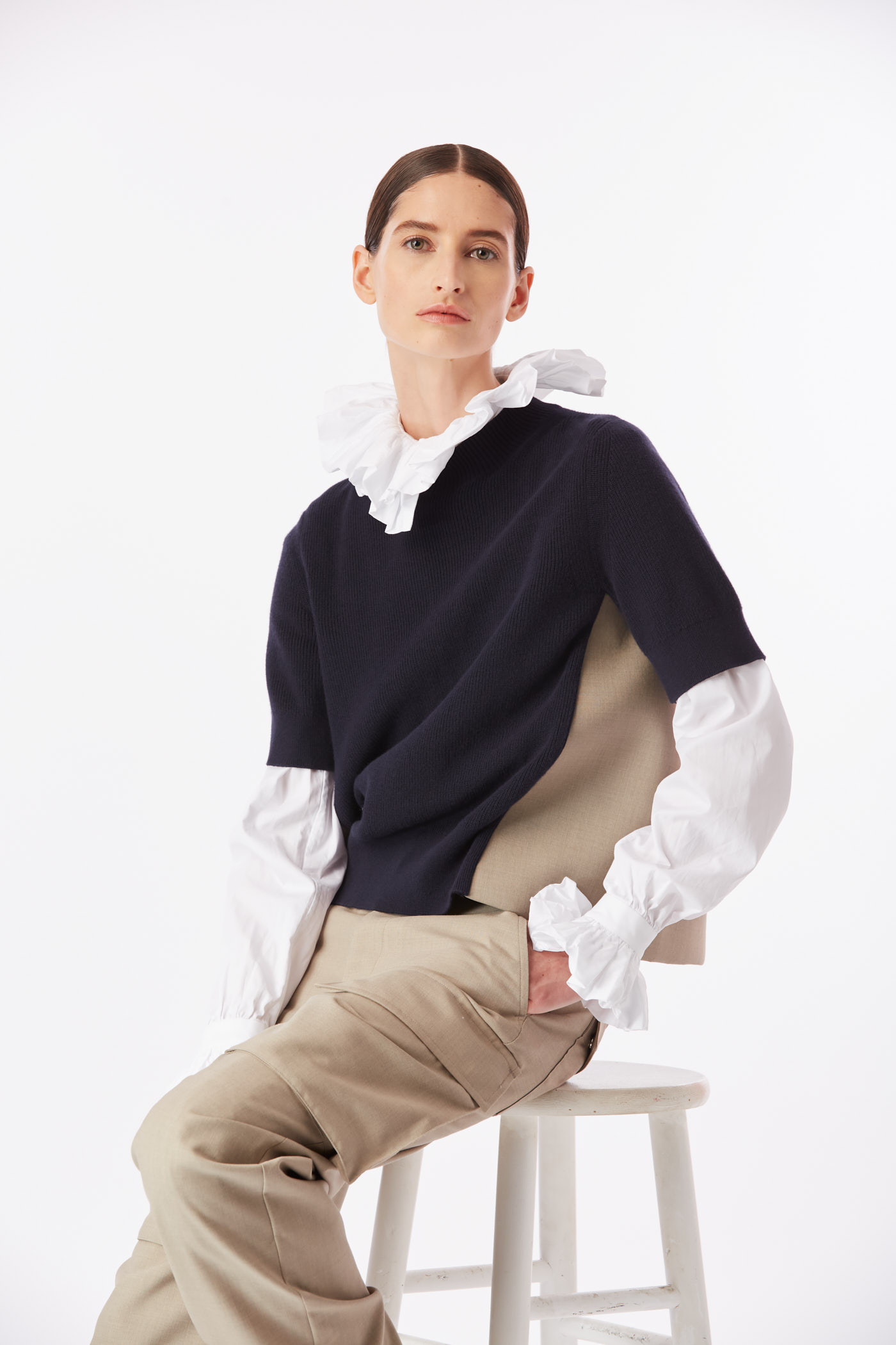 Model seated in navy sweater with exaggerated white ruffle collar during New York editorial photoshoot