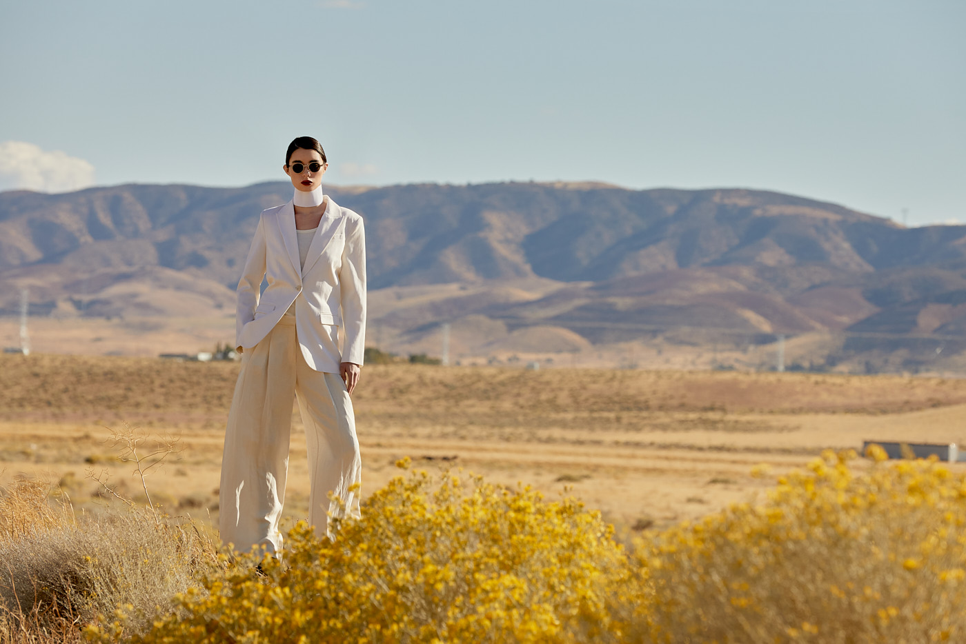 Model in structured white suit posing in front of desert mountains, photographed by New York fashion photographer Vikram Pathak