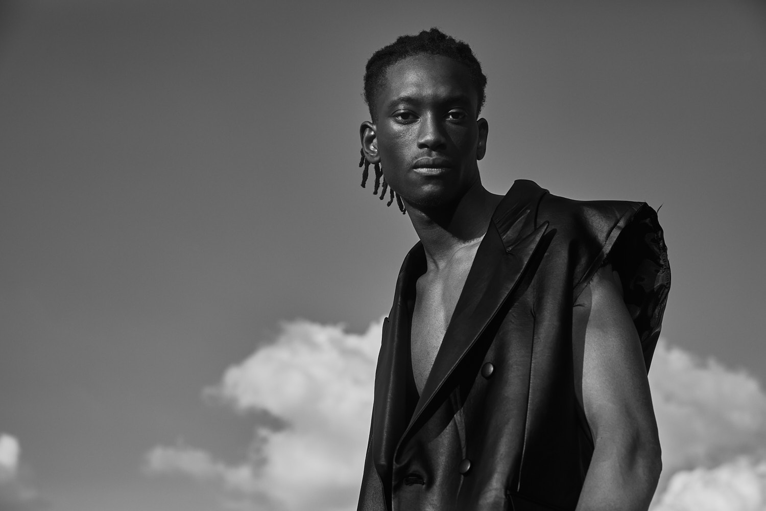 Black-and-white portrait of male model in sleeveless suit with clouds in background, photographed by Vikram Pathak.