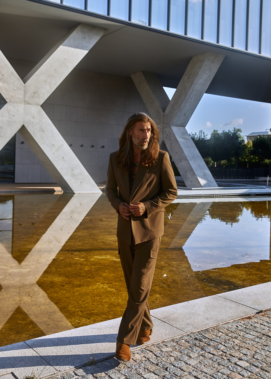 Male model in brown tailored suit walking beside water reflection at Prada Foundation Milan, photographed by Vikram Pathak.