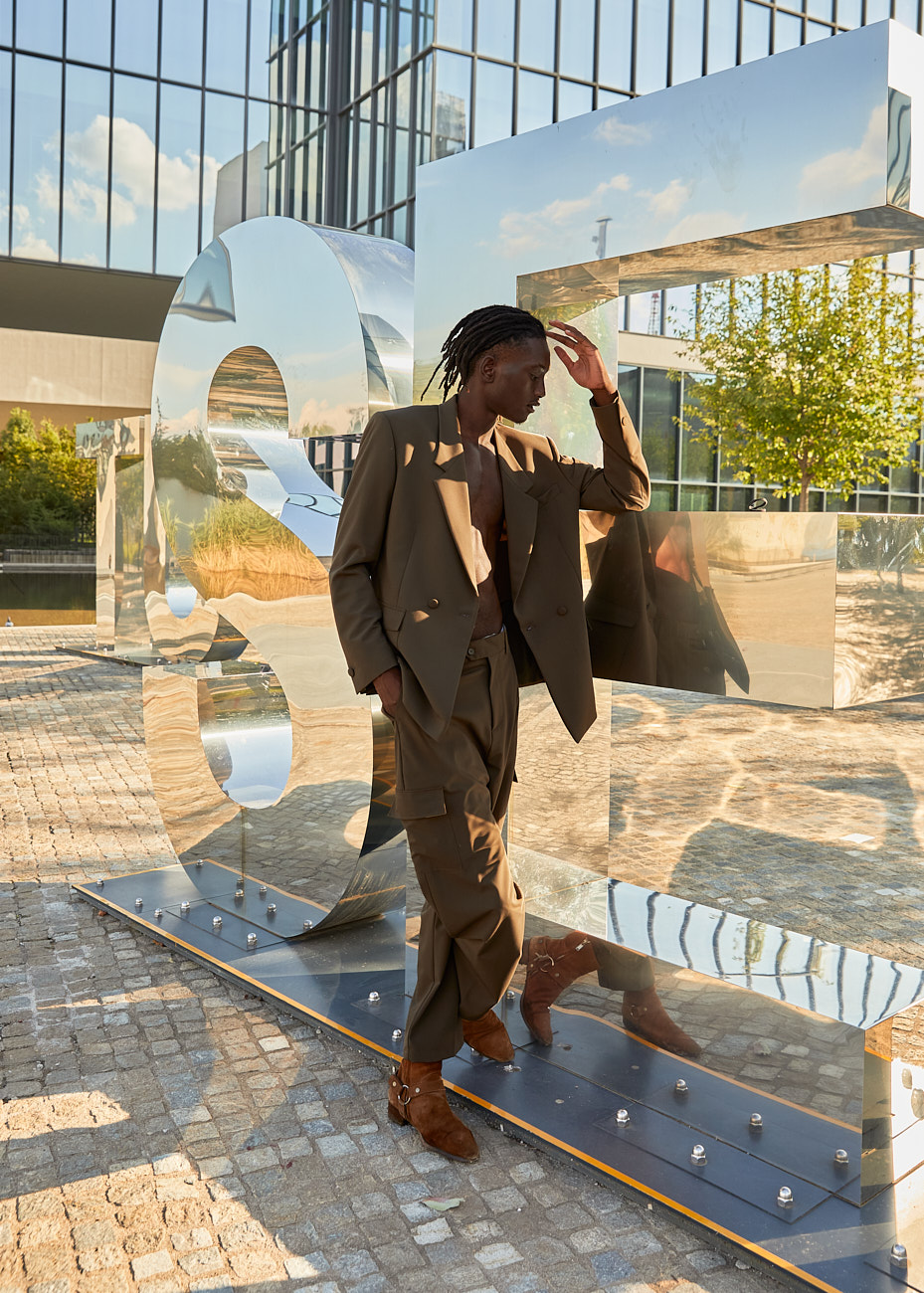 Male model posing beside metallic art sculpture, photographed by Vikram Pathak for his men’s fashion editorial.
