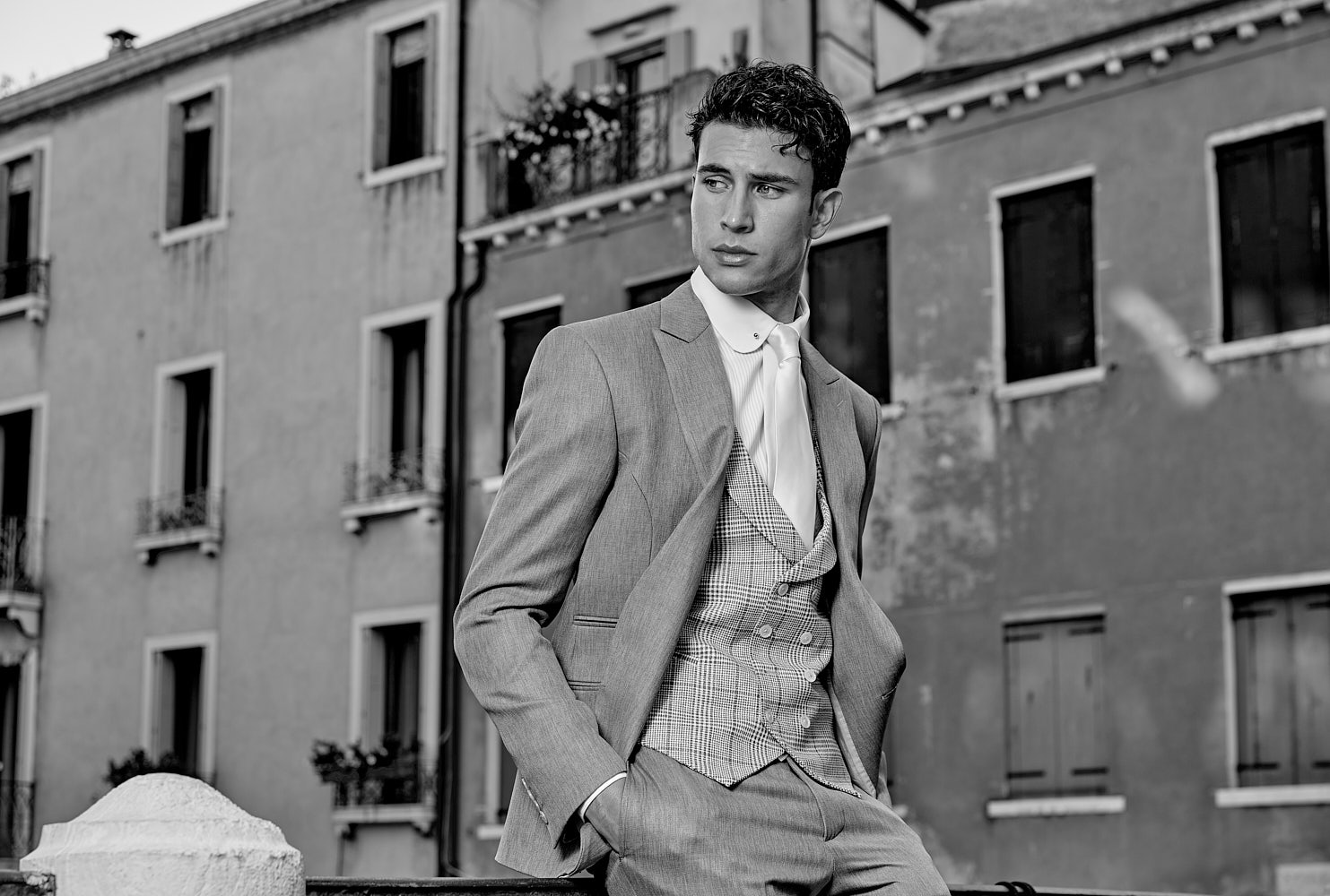 Male model wearing three-piece grey suit in black-and-white editorial portrait in Venice