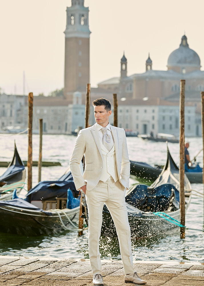 Male model in light beige suit photographed near gondolas and water reflections in Venice