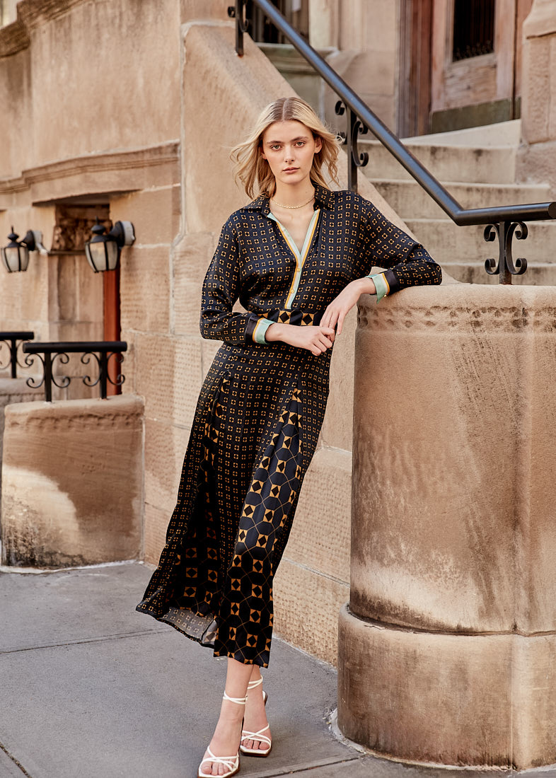 Blonde model in geometric black and gold dress leaning on urban architecture during a commercial shoot