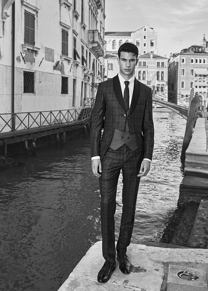 Male model in white suit posing with gondolas and Venetian domes in background