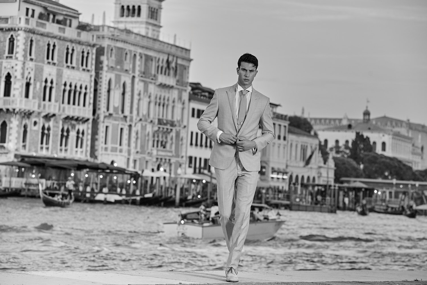 Male model walking along the Grand Canal in Venice wearing a tailored grey suit