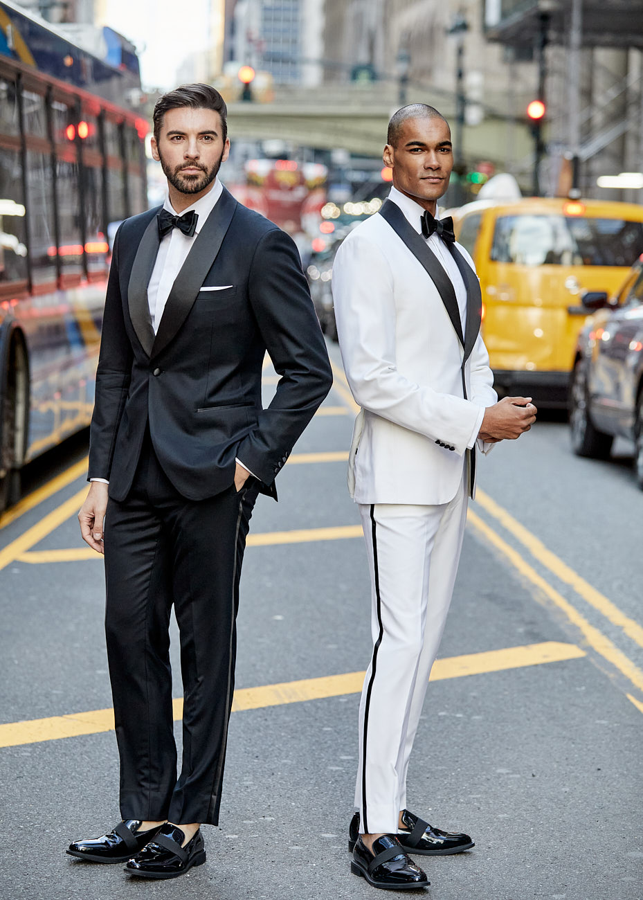 Two male models in tuxedos on NYC street flanked by yellow taxis and buses in editorial by Vikram Pathak