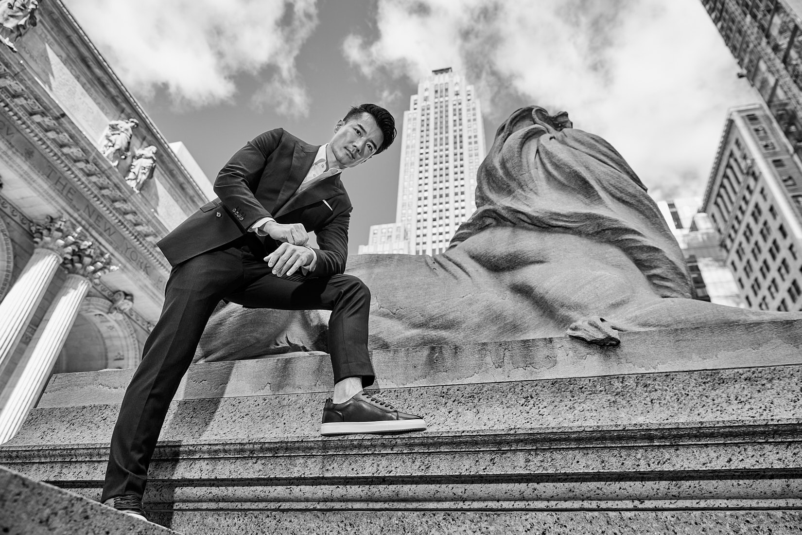 Male model posing in front of NYC lion statue in suit during fashion shoot by Vikram Pathak
