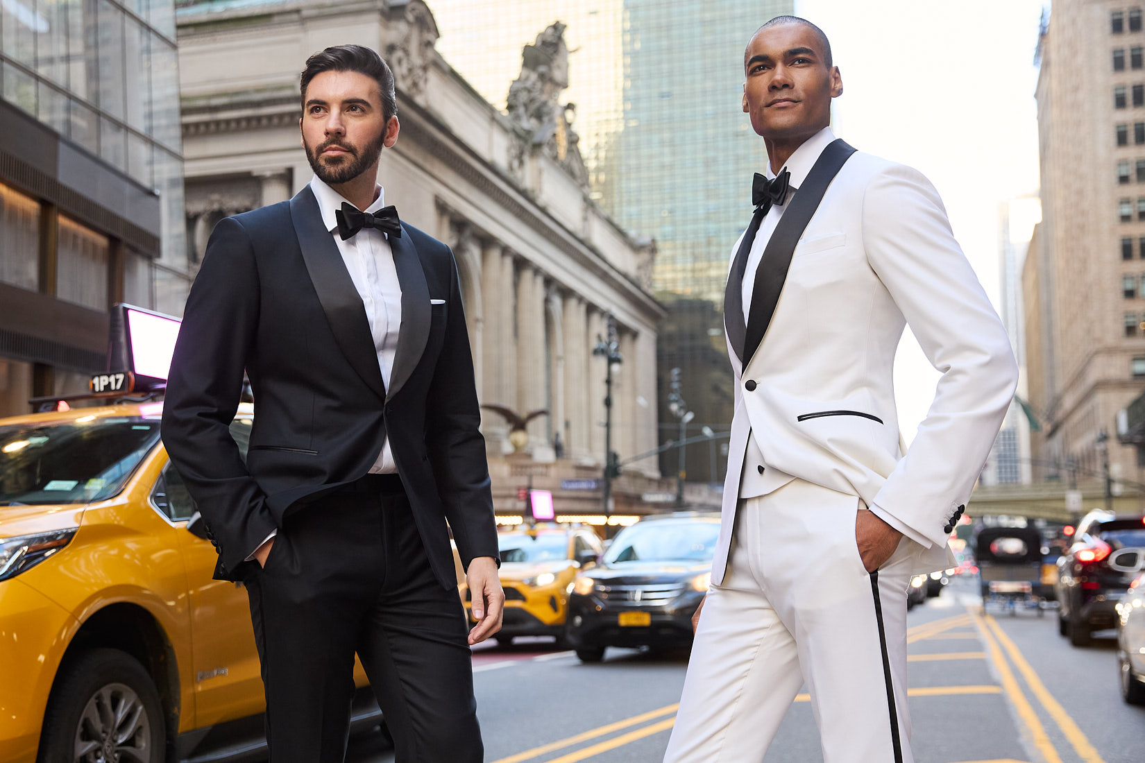 Two male models posing in white and black tuxedos in NYC street with Grand Central and taxis in background