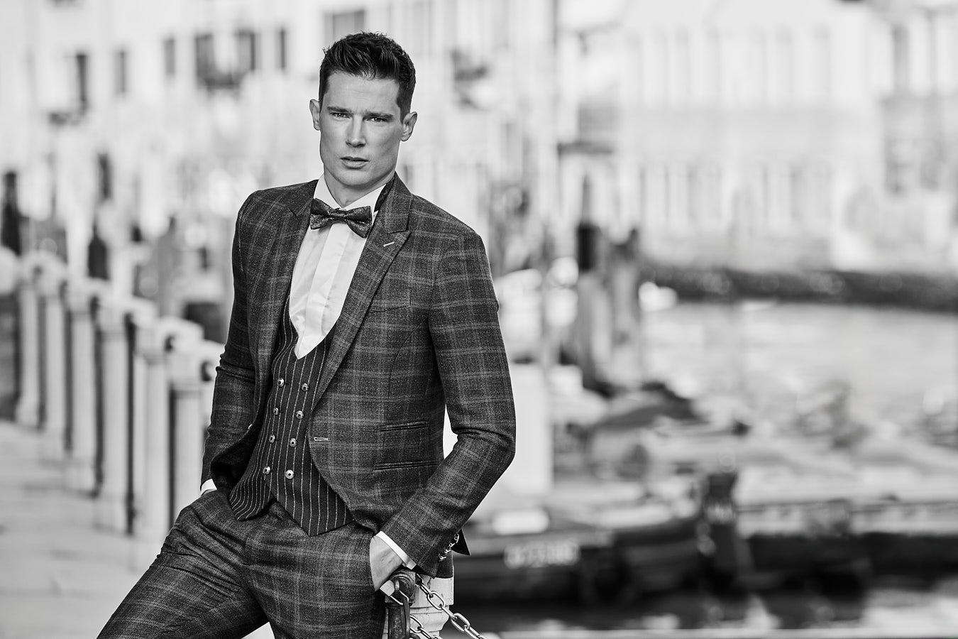 Male model in check suit with bow tie posing by canal in Venice
