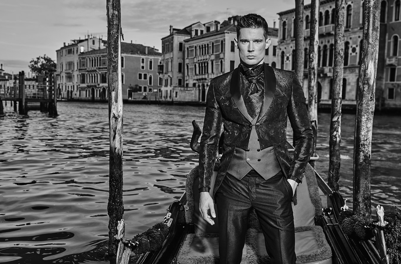 Man in embroidered tuxedo standing in gondola on canal