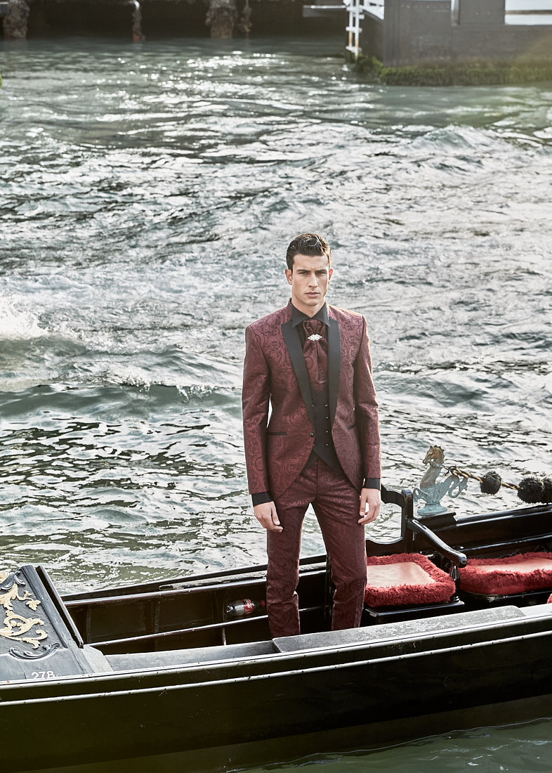 Man in burgundy tuxedo standing in gondola on Venetian water