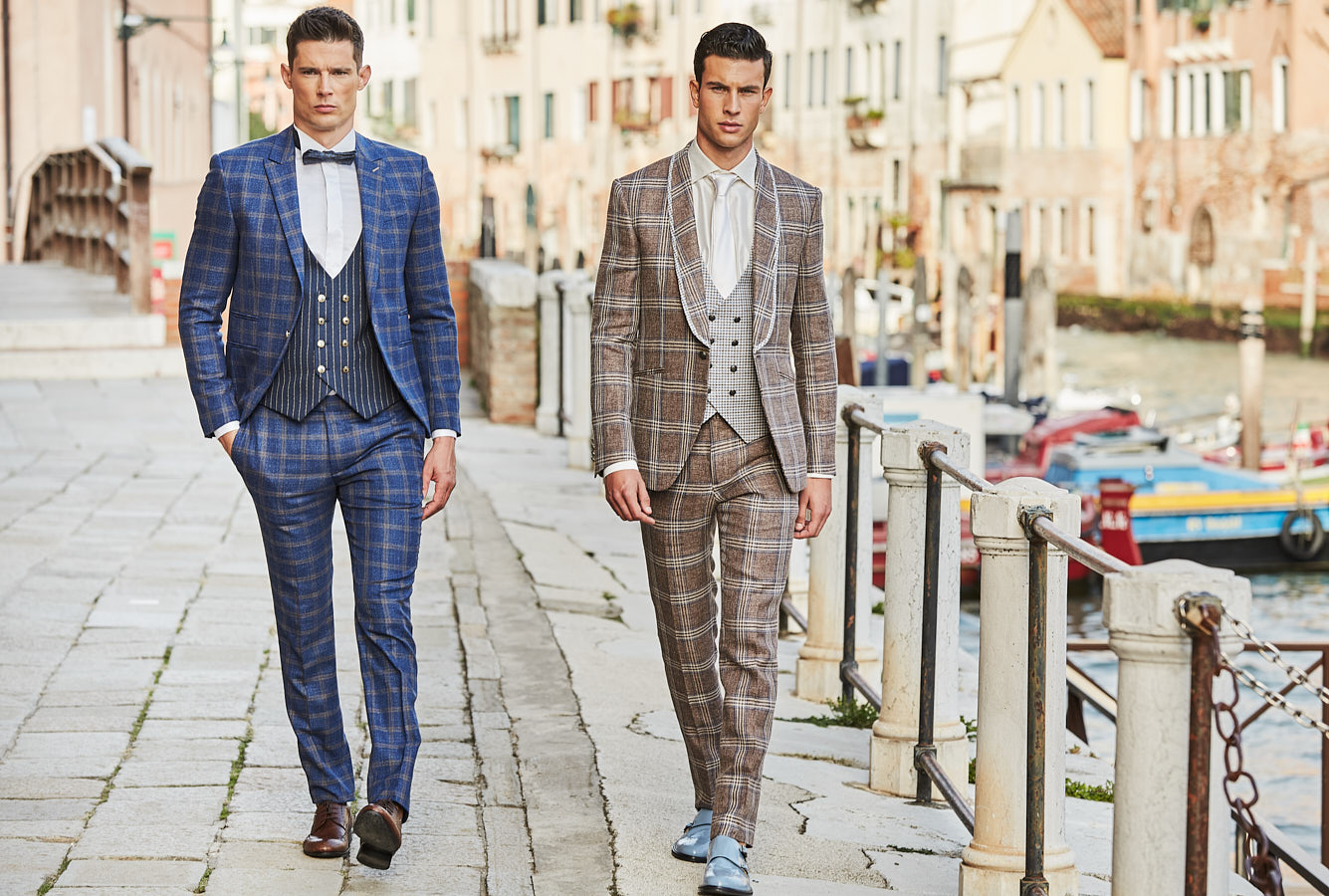 Two male models in blue and brown plaid suits walking along Venice canal
