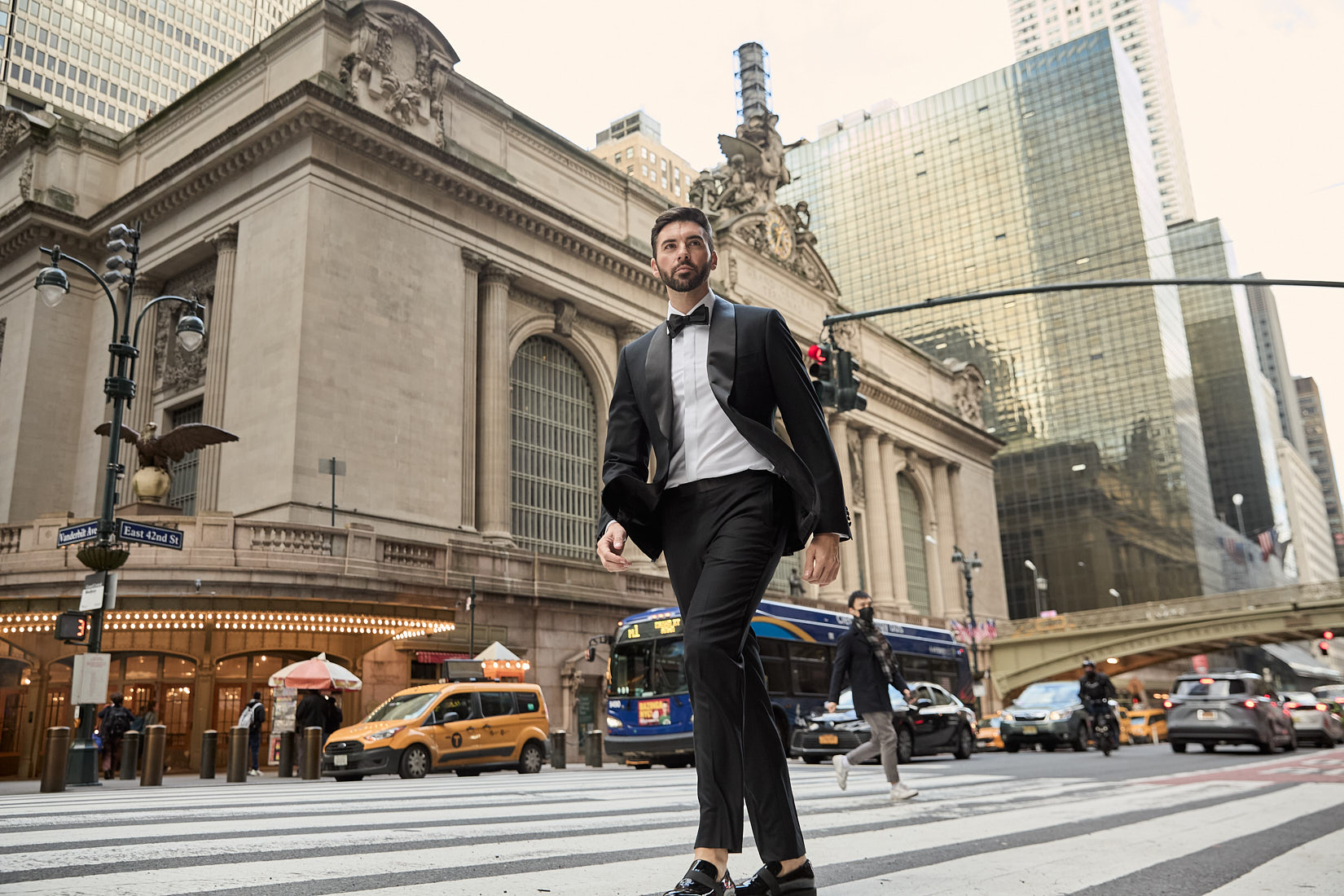 Male model in tuxedo walking across NYC crosswalk in front of Grand Central Terminal in menswear editorial shoot